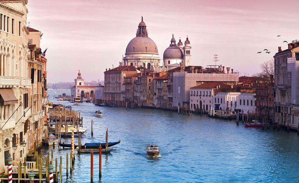 <p>Símbolo vivo do romantismo, <strong>Veneza</strong> – localizada no nordeste da Itália - inspira os sonhos de muitos casais ao redor do mundo. Canais cortados por pontes em arco, gôndolas deslizando pelas águas e palácios medievais formam a identidade desta cidade mística que está na lista de desejo de viagem da maioria das pessoas. </p>
<p>A cidade recebe turistas de diversas partes do mundo durante o ano todo. Para desfrutar da beleza dessa cidade é necessário disposição para acordar cedo e andar muito para conhecer cada canto dela. Na Praça de São Marcos - principal ponto turístico da cidade - é onde está localizada a Basílica de São Marcos e a Torre do Relógio. Aproveite para passear e fotografar a praça que é coberta pelos pombos da cidade. Desfrute também de um café da manhã no Caffè Florian, aberto em 1720 - o café mais antigo da cidade. Peça um chocolate quente e aproveite para ler um livro e namorar. Para o almoço conheça o cardápio de comida italiana e a imensa carta de vinhos do Le Bistro de Veneze. O ambiente romântico do restaurante Antico Martini é ideal para um jantar a dois. </p>
<p>Veneza também é um excelente lugar para compras. Visite o Annick Goutal, ótimo lugar para comprar perfumes e não deixe de conhecer a Bottega Veneta, onde estão localizadas as principais grifes italianas.</p>