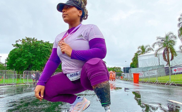 Mulher vestindo roupa fitness na cor roxa, segurando uma medalha